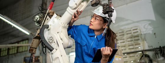 Technician woman check the robotic arm machine in the factory. Worker wearing safety helmet, glasses and uniform. Preventive maintenance to prevent breakdown. Service and repair concept.