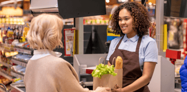 Image of a cashier handing a customer a bag of groceries they purchased 