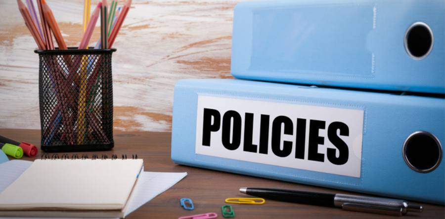 Image of pencils, pen, note pad, paper clips and policy binders on desk top