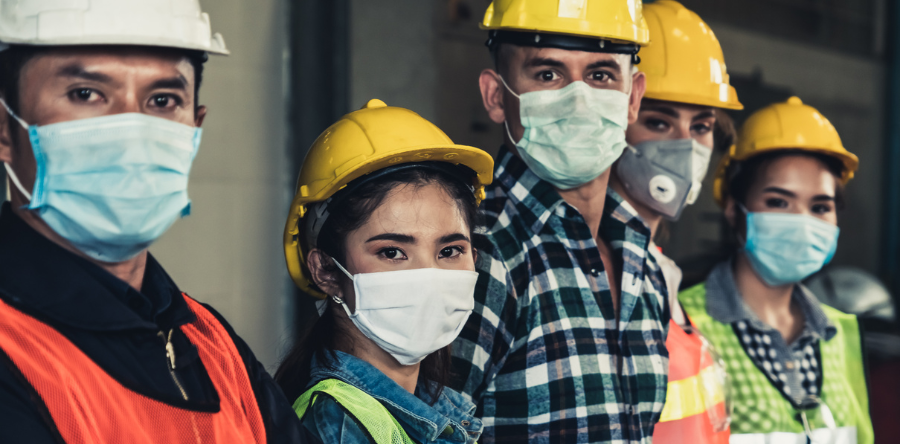 Image of warehouse workers standing in line wearing hardhats and covid masks