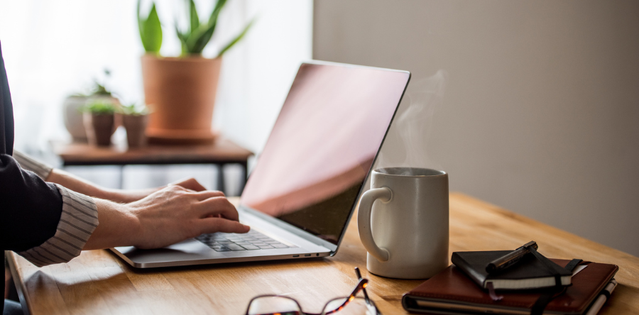Image of a person typing on a laptop with a coffee mug, glasses and notebooks on the table