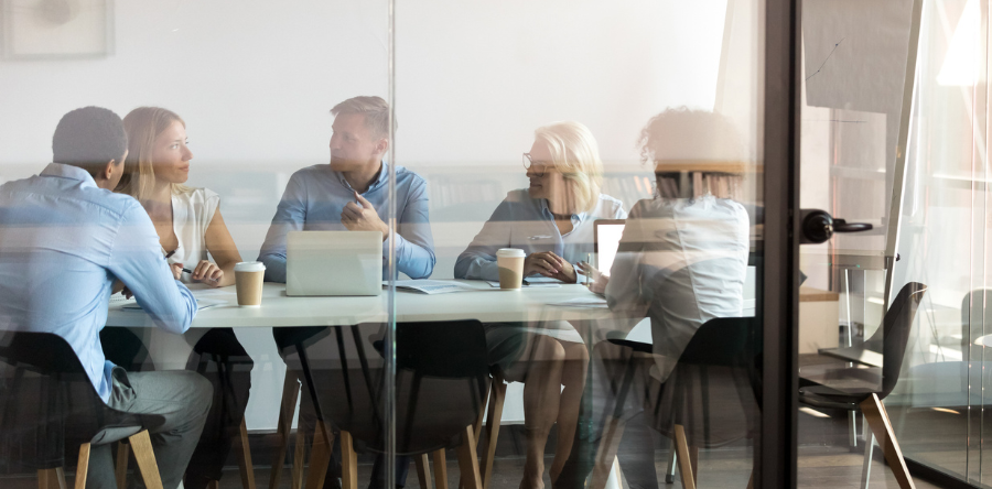 Group sitting in boardroom surrounded by glass walls having a meeting