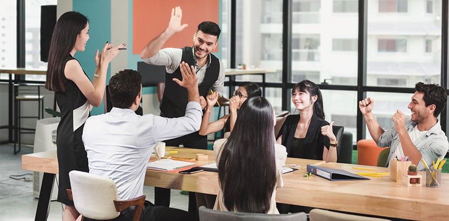 group of happy workers in a meeting sitting around table cheering for a job well done.  