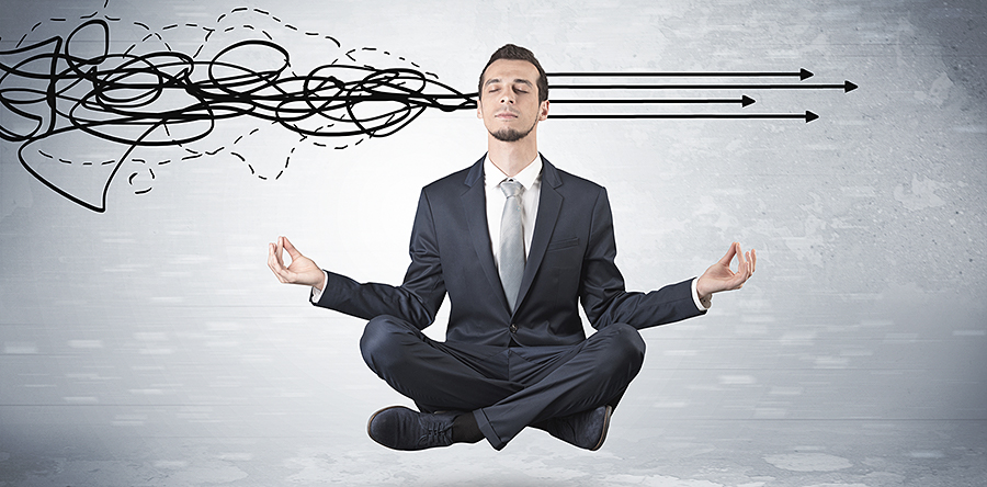 Image of a business man wearing a suit sitting down on floor with legs crossed in a yoga position