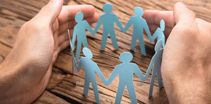 Sage green paper shaped people standing in a circle holding hands displayed on brown desk