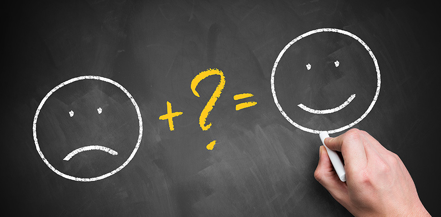 Hand writing happy face and sad face math equation on a chalkboard.