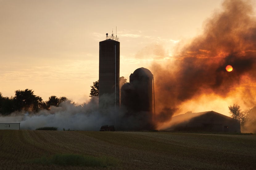 A barn and silos burining in the field against the sunset