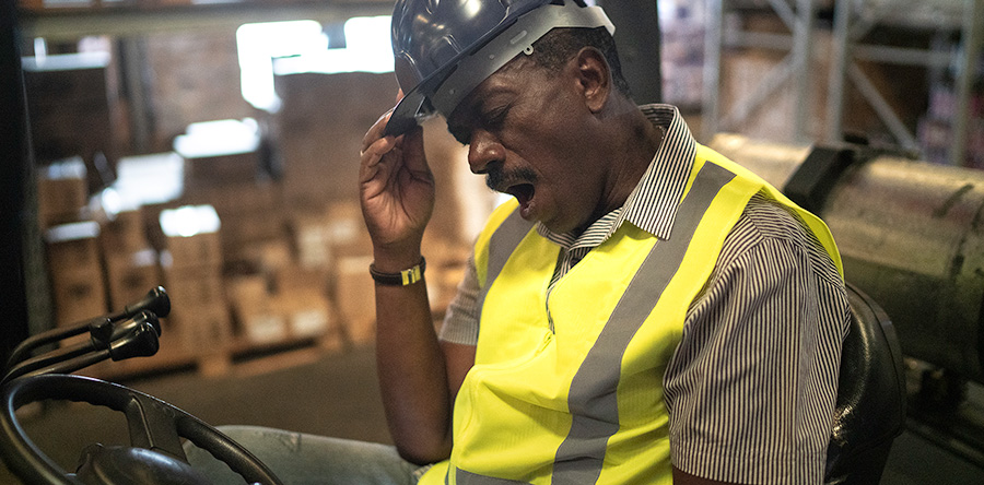 Image of a warehouse employee sitting down yawning while on the job