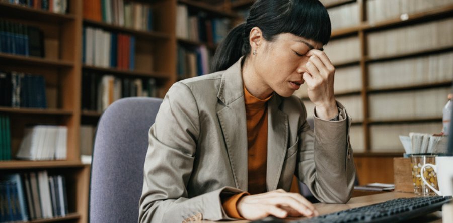 Image of a woman sitting at her desk with hand on top of head and eyes closed