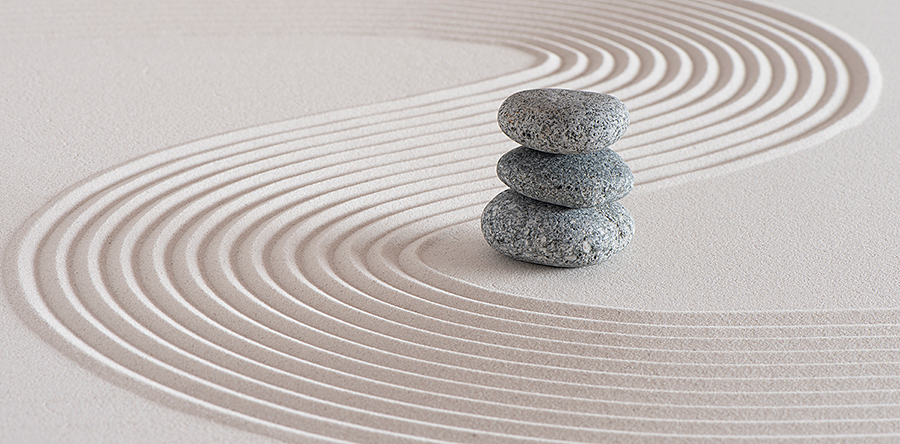 Image of three stacked stones sitting on top of light brown sand with swirl sand lines beside it