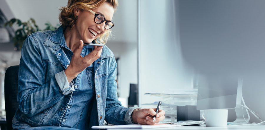 Image of a female worker sitting a desk holding a phone and taking notes