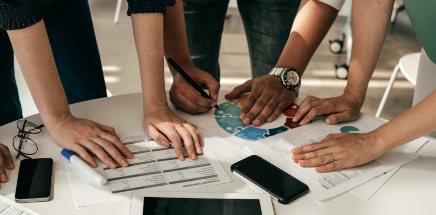 Image of three workers huddling around a circle table with hands on top of it having a meeting