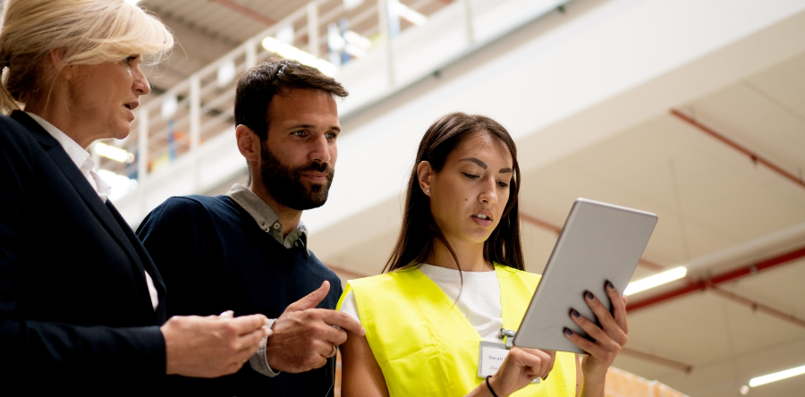 Image of co-workers standing in an office having a meeting while looking at a tablet.  