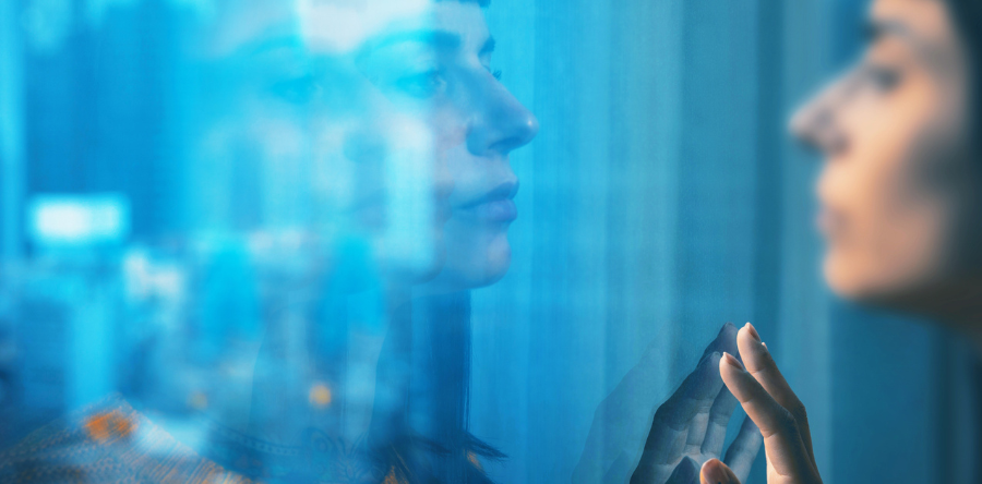 Image of a woman standing by a window with hand rested on glass looking outside 