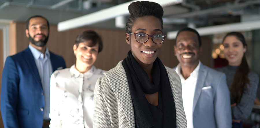 Image of two males and three woman standing in an office room smiling representing diversity