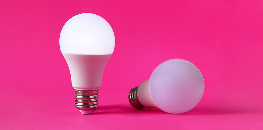Image of white light blubs one standing upright and one laying down in a bright pink background