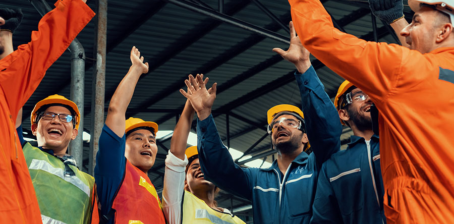 group of smiling happy construction workers gathered in a circle in warehouse with hands in air