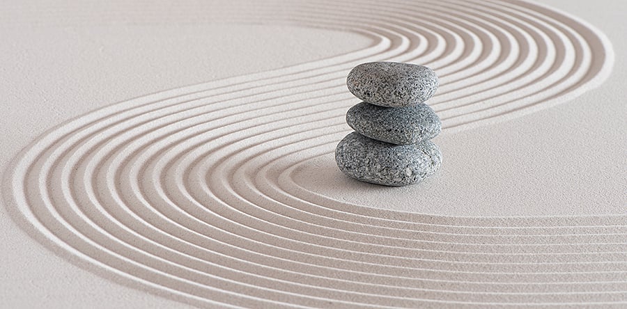 Image of three stacked stones sitting on top of light brown sand with swirl sand lines beside it 